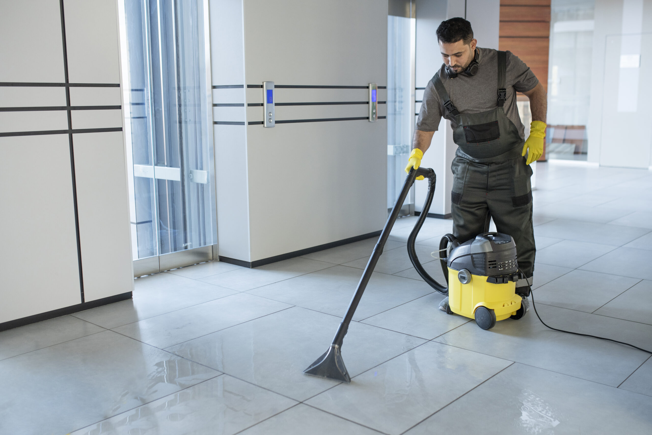 professional janitor providing commercial cleaning warehouse services by industrial vacuuming a large polished floor.